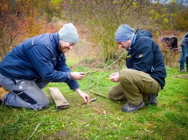 Zwei Personen arbeiten mit Ästen auf einer Wiese beim Überlebenstraining