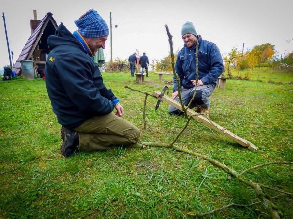 Zwei Personen bauen eine Holzvorrichtung aus Ästen und einem Messer
