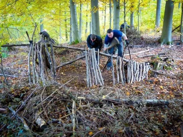 Zwei Personen bauen eine Struktur aus Ästen im Wald beim Überlebenstraining