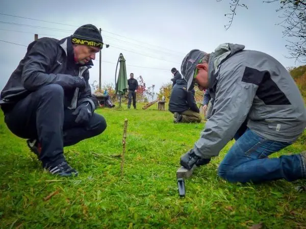 Zwei Personen bearbeiten einen Stock mit einem Messer auf einer Wiese