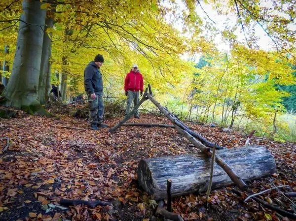 Zwei Personen betrachten eine selbstgebaute Seilbrücke aus Ästen und einem Baumstamm