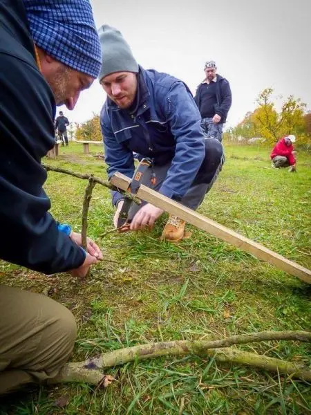 Zwei Personen binden eine Holzstange mit Schnüren an einen Ast