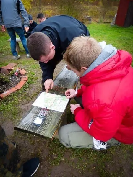 Zwei Personen studieren eine Karte auf einer Holzbank, während andere im Hintergrund aktiv sind