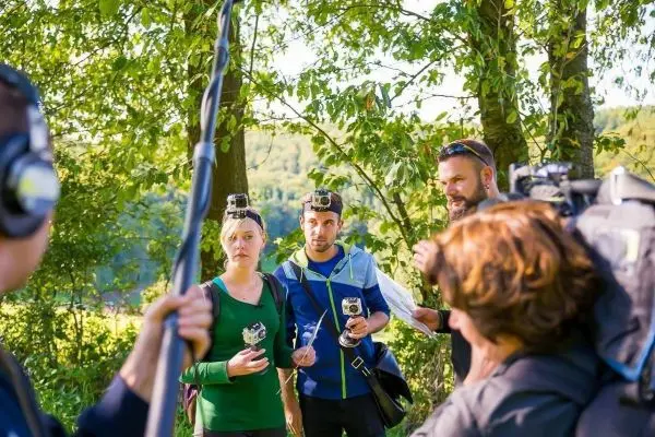 Drei Personen mit Action-Kameras stehen unter Bäumen und sprechen miteinander