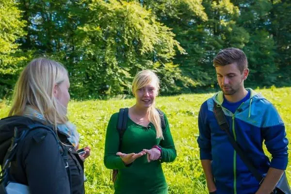 Drei Personen stehen in einer Wiese und diskutieren miteinander