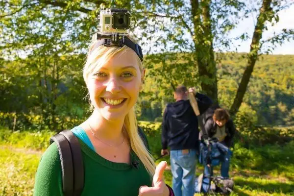 Frau mit Actionkamera auf dem Kopf gibt Daumen hoch, im Hintergrund zwei Personen mit Kamera
