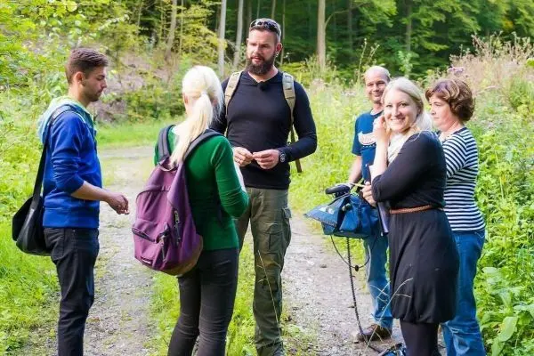 Gruppe diskutiert auf einem Waldweg, Ausrüstung und Rucksäcke sind sichtbar
