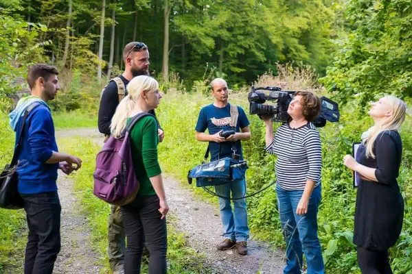 Gruppe diskutiert im Wald, während eine Person mit Kamera filmt