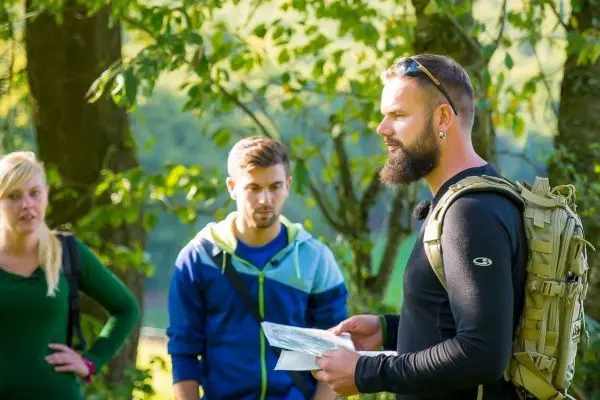 Mann mit Karte erklärt Orientierungstechniken an zwei Zuhörern im Freien