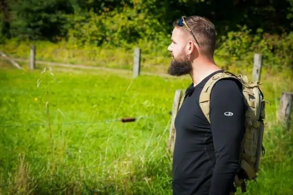 Mann mit Rucksack steht an einem Feldrand und schaut nach rechts