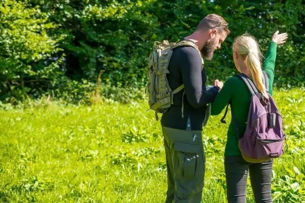 Mann mit Rucksack zeigt auf eine Richtung, Frau hört aufmerksam zu