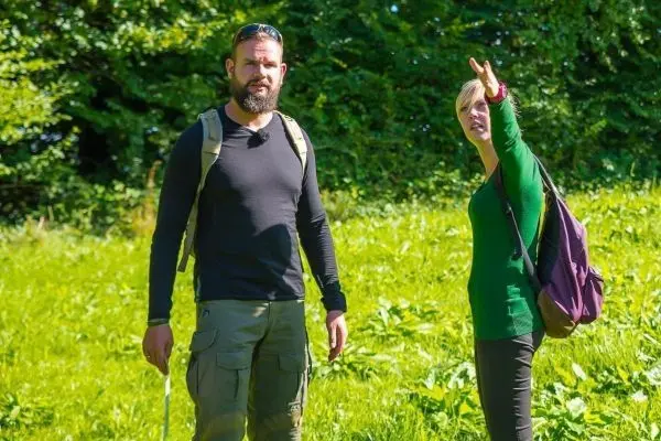 Zwei Personen stehen in einer Wiese und zeigen in verschiedene Richtungen