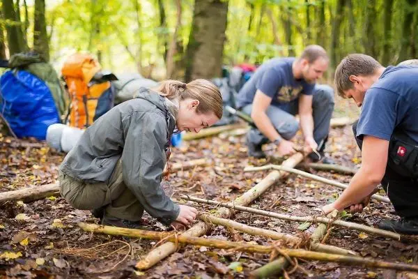 Drei Personen bauen eine Holzstruktur aus Ästen im Wald