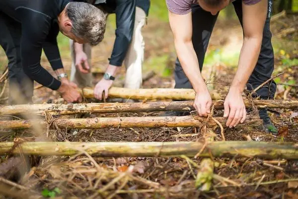 Drei Personen bauen eine Struktur aus Ästen im Wald auf