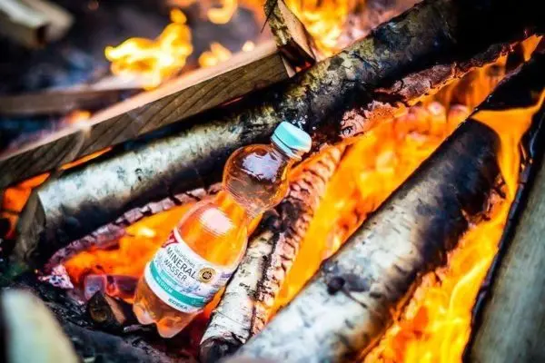 Flasche steht zwischen brennenden Holzscheiten