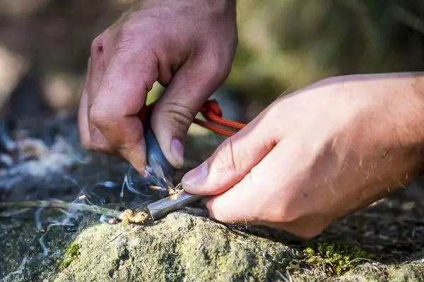 Hände erzeugen Funken mit Feuerstahl auf einem Stein beim Survival Training