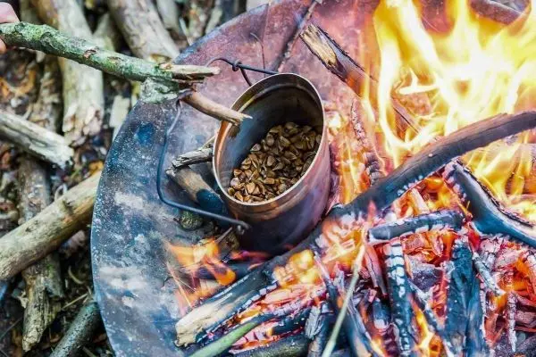 Kessel hängt über dem Feuer, während Holzstücke brennen