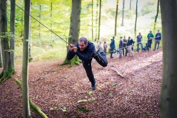 Person schwingt an einer Seilüberquerung zwischen Bäumen beim Survival Training