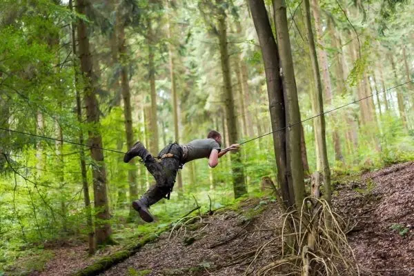Person schwingt sich an einem Seil zwischen Bäumen