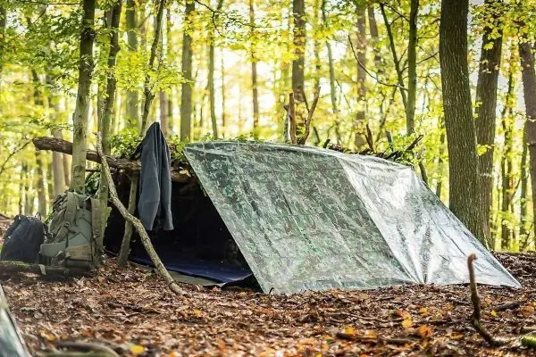 Tarp-Notunterkunft aus Ästen und Plane im Wald, Rucksack daneben