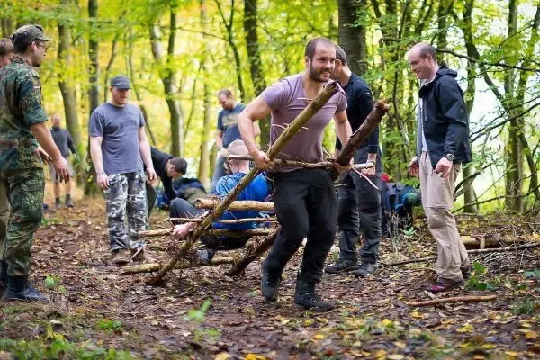 Teilnehmer tragen eine selbstgebaute Trage aus Ästen durch den Wald