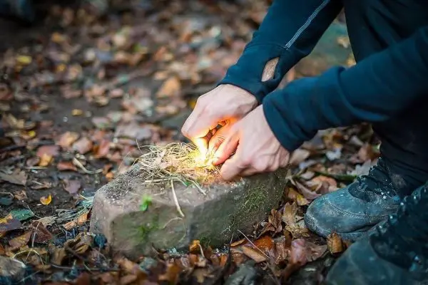 Zunder glimmt auf einem Stein, während Feuerstahl Funken erzeugt