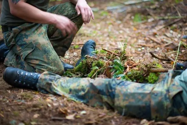 Zwei Personen in Tarnkleidung arbeiten am Boden mit Pflanzenmaterial
