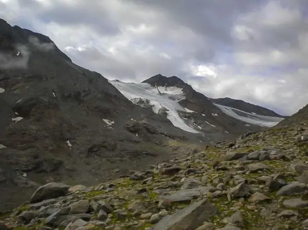 Berglandschaft mit Gletscher und steiniger Untergrund unter bewölktem Himmel