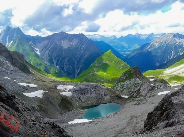 Berglandschaft mit grünen Hängen, schneebedeckten Gipfeln und einem kleinen See im Tal