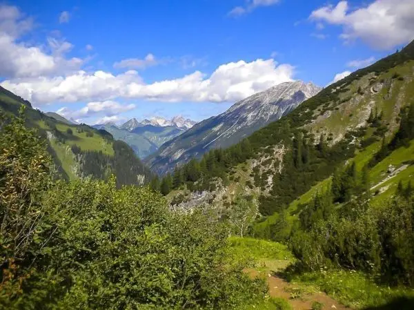 Berglandschaft mit grünen Hängen und bewaldeten Flächen unter blauem Himmel