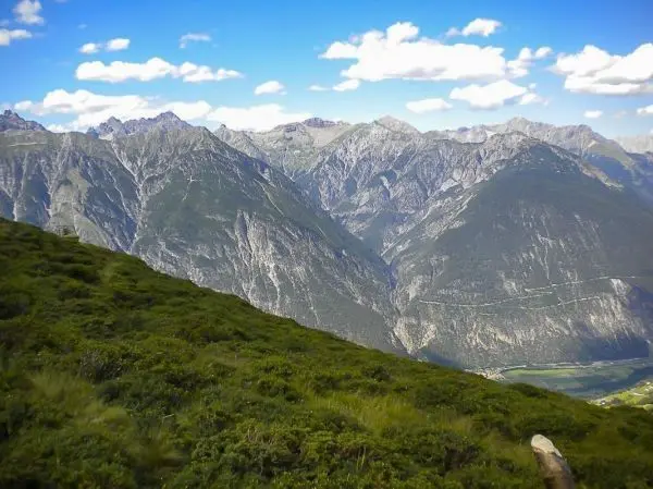 Berglandschaft mit grünen Hängen und schroffen Gipfeln unter blauem Himmel