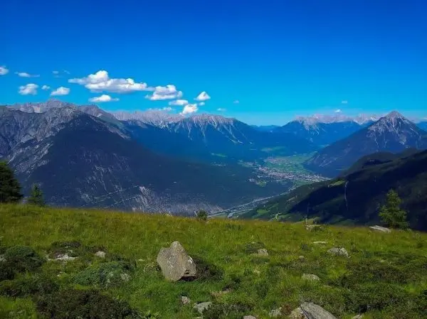 Berglandschaft mit grünen Wiesen, Felsen und schneebedeckten Gipfeln unter blauem Himmel