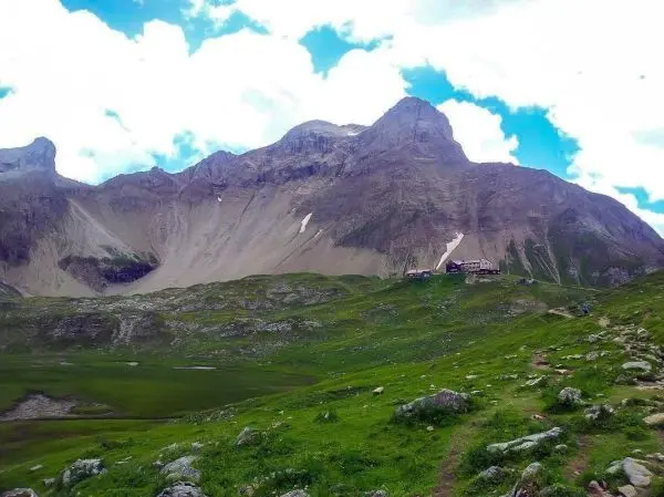 Berglandschaft mit grünen Wiesen und einer Berghütte im Vordergrund