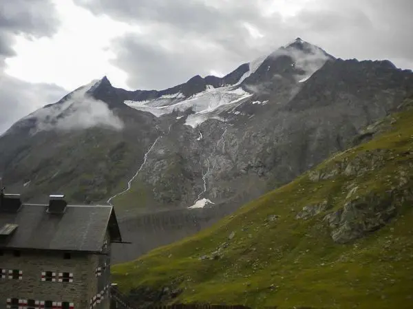 Berglandschaft mit schneebedecktem Gipfel und bewölktem Himmel über einer Hütte