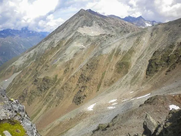 Berglandschaft mit steilen Hängen und felsigen Gipfeln unter bewölktem Himmel