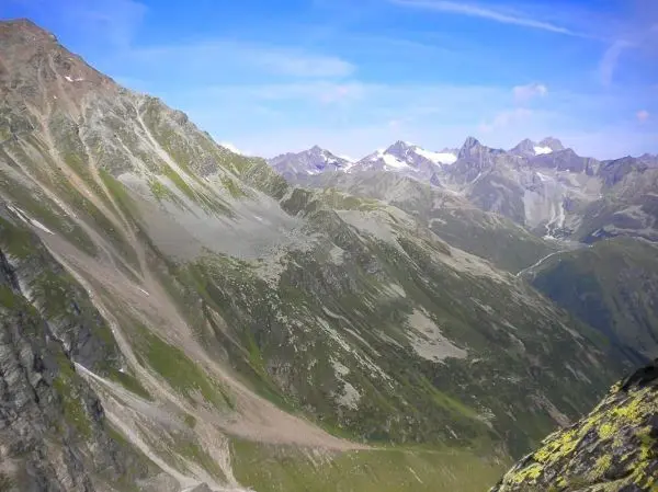 Berglandschaft mit steilen Hängen und schneebedeckten Gipfeln im Hintergrund