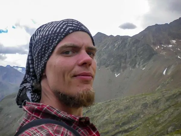 Ein Mann mit Kopftuch und kariertem Hemd steht vor einer Berglandschaft