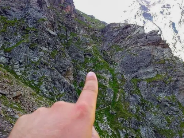 Finger zeigt auf einen schmalen Pfad zwischen Felsen und Gras