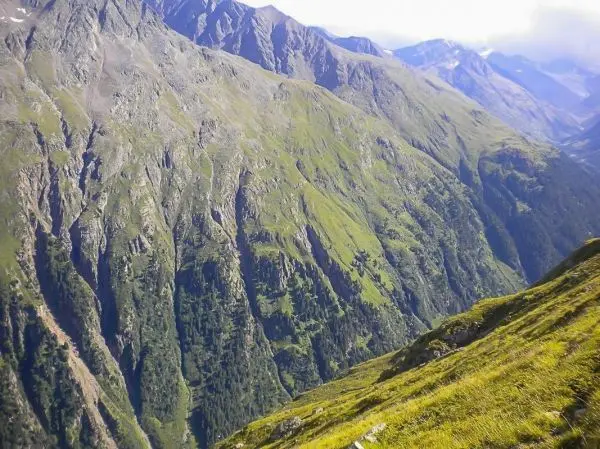 Grüne Berghänge mit steilen Felsen und bewaldeten Tälern im Hochgebirge
