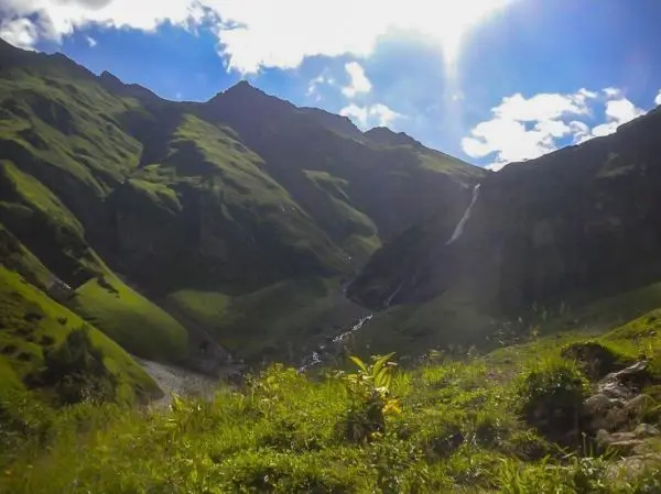 Grüne Berglandschaft mit einem Wasserfall und einem kleinen Fluss im Tal