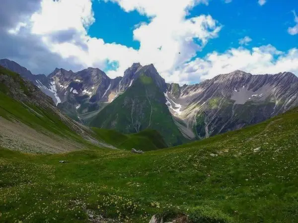 Grüne Wiesen und steile Berge unter einem bewölkten Himmel