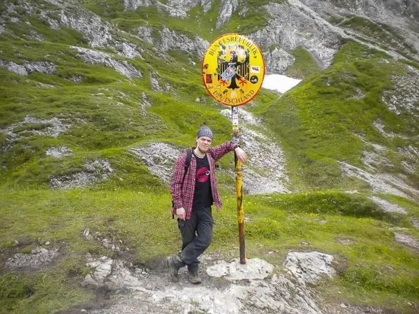 Mann lehnt an einem Wegweiser in einer bergigen Landschaft