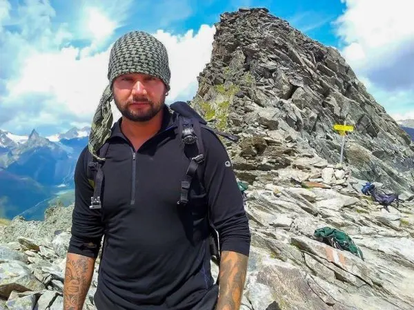 Mann mit Rucksack steht auf felsigem Gelände vor einem Berggipfel