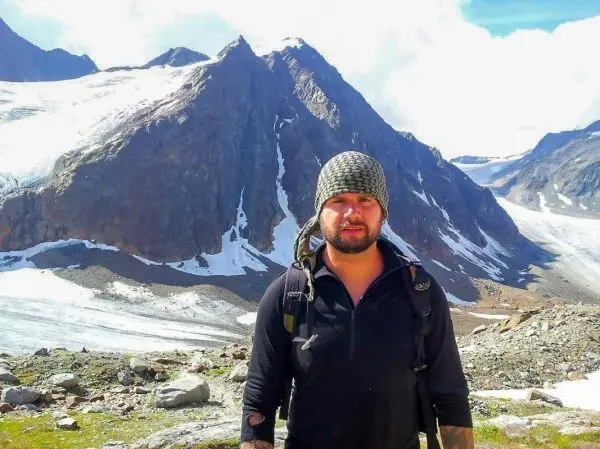 Mann mit Rucksack steht vor schneebedeckten Bergen und felsigem Gelände