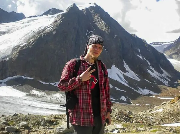 Mann posiert vor schneebedeckten Bergen mit Rucksack und gestikuliert