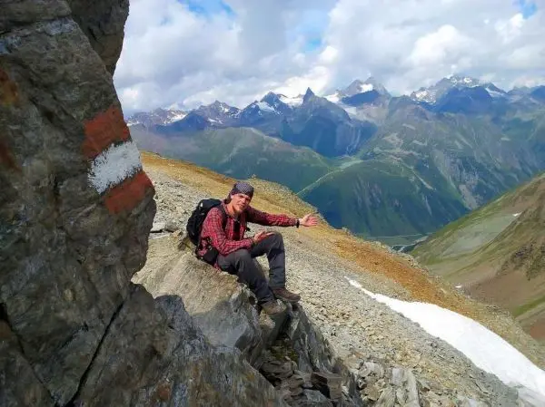 Mann sitzt auf einem Felsen und zeigt in die Ferne, Berglandschaft im Hintergrund