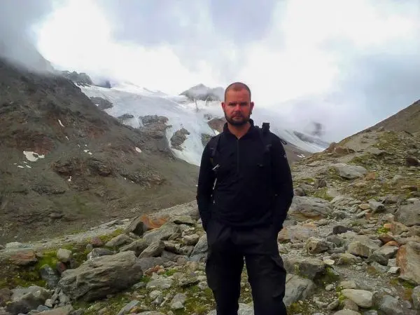 Mann steht auf einem steinigen Gelände mit Bergen im Hintergrund