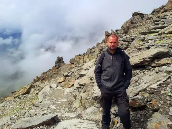 Mann steht auf einem steinigen Pfad in den Bergen, Wolken ziehen vorbei