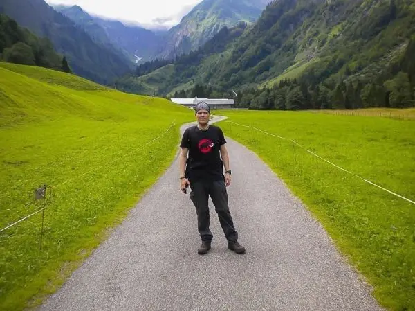 Mann steht auf einem Weg in einer grünen Landschaft mit Bergen im Hintergrund