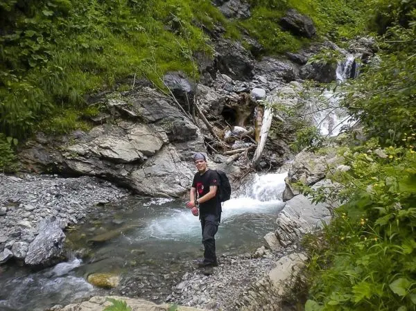 Mann steht im Wasser eines kleinen Baches, umgeben von Felsen und Pflanzen